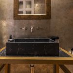 Baño de cortesía con lavabo de mármol negro y grifería vintage — fotografía inmobiliaria de piso reformado en Chueca